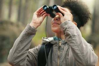 Hiking, forest and woman with binocular watch nature scenery, view or bird watching while trekking