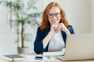 Pleased cheerful female economist develops financial startup project, poses in office interior