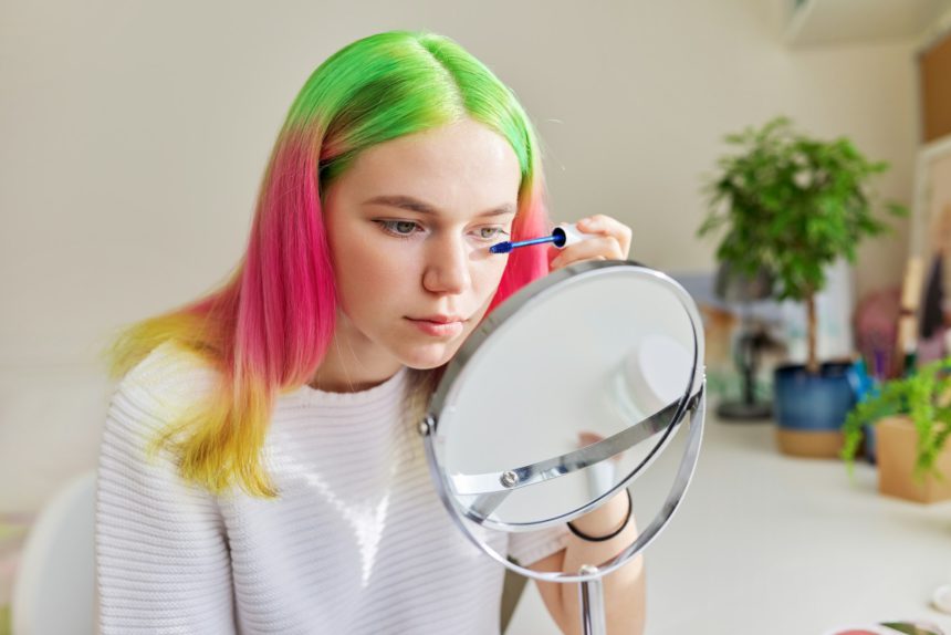 Teen girl with colored dyed hair dyeing eyelashes with mascara